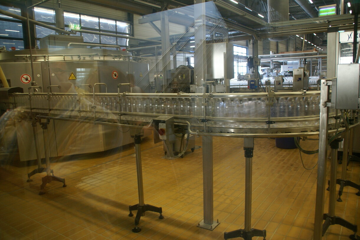 Stainless conveyor line carrying bottles through a modern European beverage bottling plant